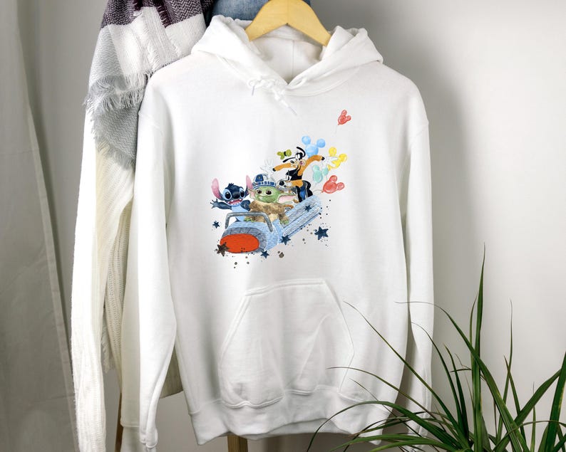 May include: White hooded sweatshirt with a colorful graphic print of Stitch, Baby Yoda, and Mickey Mouse riding in a spaceship. The graphic is surrounded by stars and hearts.