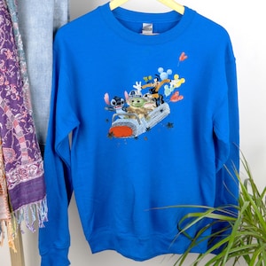 May include: A royal blue sweatshirt with a graphic print of Stitch, Baby Yoda, and Mickey Mouse riding in a spaceship. The characters are smiling and waving.