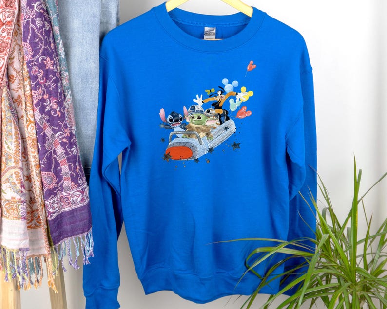 May include: A royal blue sweatshirt with a graphic print of Stitch, Baby Yoda, and Mickey Mouse riding in a spaceship. The characters are smiling and waving.