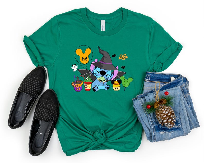 May include: Green t-shirt featuring a cartoon Stitch dressed as a witch, holding a smaller Stitch. The shirt has a Halloween theme with other cartoon characters and a Mickey Mouse balloon.