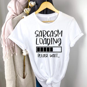 May include: White t-shirt with black text that reads "Sarcasm Loading... Please Wait..." with a black progress bar.