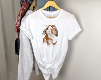 May include: White t-shirt with a brown and white rabbit illustration. The rabbit has brown fur with white markings and is looking to the left.