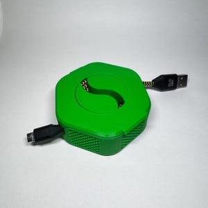 May include: A bright green USB cable organizer with a hexagonal shape. The cable is black and yellow. The USB connector is black with white text. The organizer has a slot for the cable to pass through.