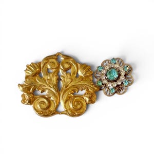 Peut inclure: Deux broches vintage sur fond blanc. L'une est une broche dorée ornée en forme de feuille. L'autre est une broche en forme de fleur avec une pierre turquoise centrale et des pierres claires et turquoise environnantes.