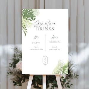 Peut inclure: Un panneau blanc sur un chevalet en bois, affichant "Signature Drinks" en écriture cursive. Le panneau détaille deux recettes de cocktails, "Paloma" et "Mezcalita", avec leurs ingrédients. Des feuilles tropicales vertes ornent les coins du panneau.