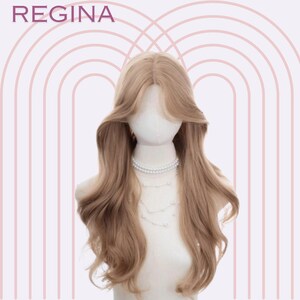 May include: A long, wavy, light brown wig with a side part. The wig is styled with loose waves and is worn on a white mannequin head.