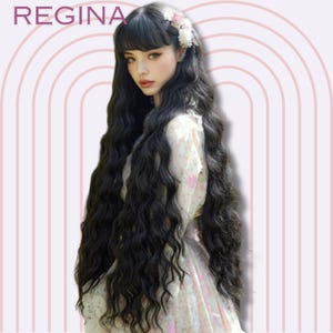 May include: A woman with long, wavy black hair, styled with bangs and a floral hair accessory. The image features the word "REGINA" at the top left. The background has a pink and white arched design.