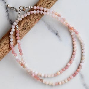 May include: A double-strand necklace made of pink and white opal beads. The necklace has a silver clasp.