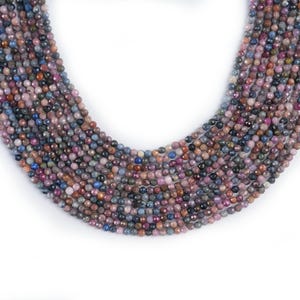 May include: A strand of multi-colored gemstone beads. The beads are round and have a faceted finish. The colors of the beads include pink, blue, purple, and brown.