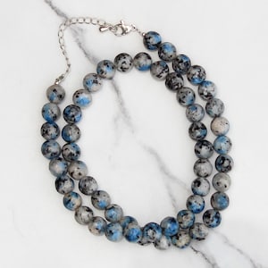 May include: A double-strand necklace made of blue and gray speckled round beads. The necklace has a silver clasp.