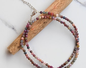 May include: A delicate multi-colored gemstone necklace with a silver clasp. The necklace is made of small, faceted beads in shades of pink, purple, blue, and green.