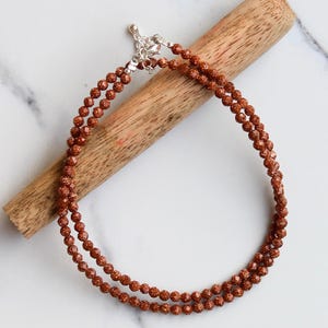 May include: A double strand necklace made of small, round, brown beads. The beads have a sparkly, textured surface. The necklace has a silver clasp.