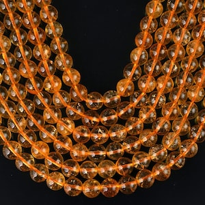 May include: A strand of round, orange citrine beads. The beads are smooth and polished, with a slight shimmer. The strand is approximately 18 inches long.