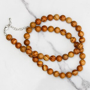 May include: A brown and beige gemstone beaded necklace with a silver clasp. The beads are round and have a striped pattern.