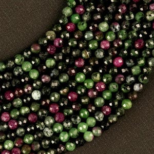 May include: A strand of faceted green and pink gemstone beads. The beads are round and have a polished finish.