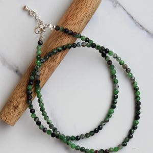 May include: A double strand necklace made with green, black, and pink gemstone beads. The necklace is made with small, round beads and has a silver clasp.