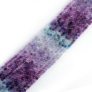 May include: A strand of faceted gemstone beads in shades of purple, blue, and white. The beads are round and have a smooth, polished finish.