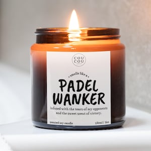 May include: A lit scented soy candle in a brown glass jar. The label reads "PADEL WANKER" with the text "infused with the tears of my opponents and the sweet scent of victory." The candle is 6 oz.