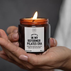 May include: A lit soy candle in an amber glass jar with a white label that reads COU COU, SMELLS LIKE I'M IN MY REFORMER PILATES ERA, infused with the sweet aroma of grip socks, a shaky core, and a few more pulses, 180ml/6oz.