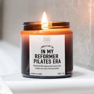 May include: A lit scented soy candle in a dark amber glass jar with a white label that reads: COU COU, SMELLS LIKE I'M IN MY REFORMER PILATES ERA, infused with the sweet aroma of grip socks, a shaky core, and a few more pulses. 180ml / 6oz.