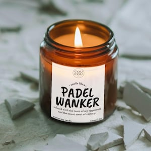 May include: A lit scented soy candle in a brown glass jar. The label reads "PADEL WANKER" with the text "smells like a..." above and "infused with the tears of my opponents and the sweet scent of victory" below. The candle is 100ml / 6oz.