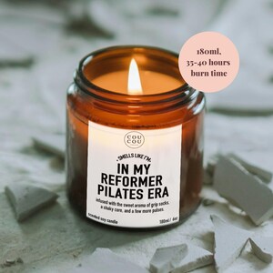 May include: A lit scented soy candle in an amber glass jar with a white label reading Cou Cou, Smells Like I'm In My Reformer Pilates Era, infused with the sweet aroma of grip socks, a shaky core, and a few more pulses. It is 6oz, 180ml, 35-40 hours burn time.