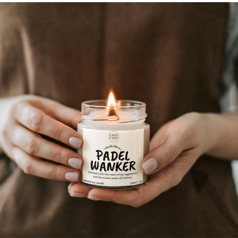 May include: A lit scented soy candle in a clear glass jar. The label reads "PADEL WANKER" with additional text. The candle is held in two hands. The candle is 4 oz.