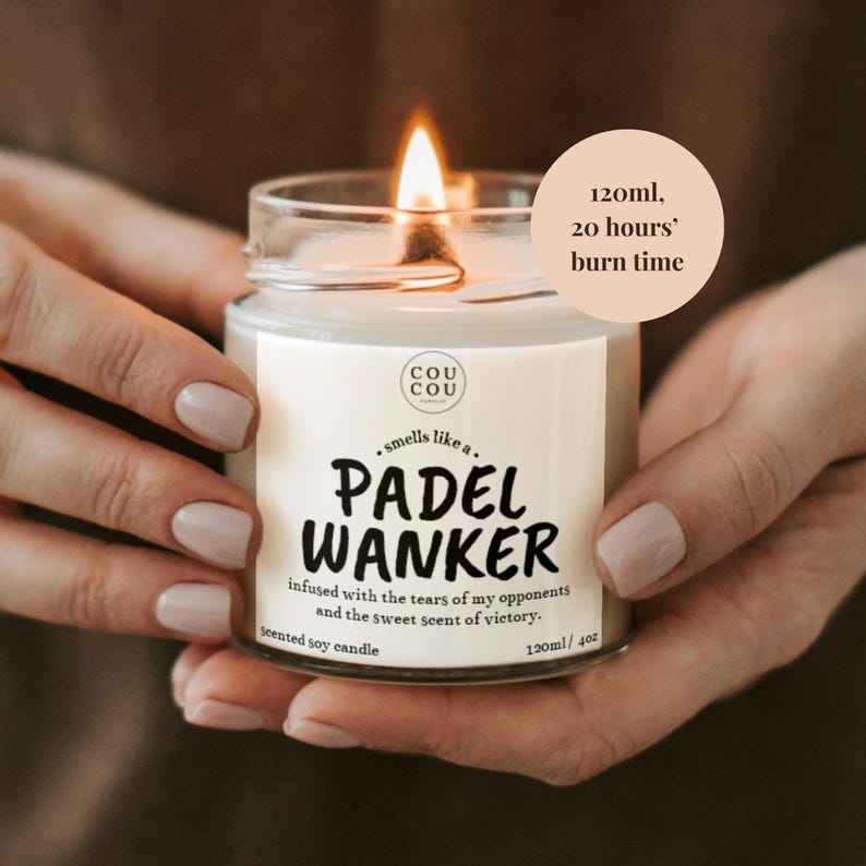 May include: A lit scented soy candle in a glass jar. The label reads "PADEL WANKER" with text about the scent. The candle has a burn time of 20 hours and contains 120ml / 4oz of wax.