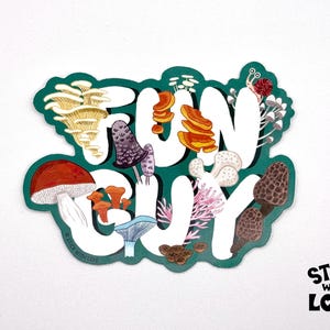 May include: A die-cut sticker featuring the white text FUN GUY set against a dark green background. The design is decorated with various illustrated mushrooms in shades of red, orange, brown, and white, along with a small snail and coral.