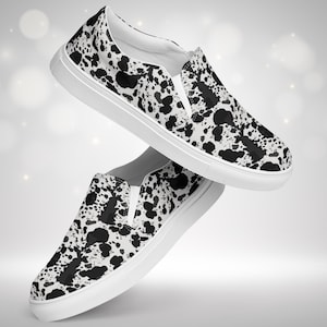 May include: A pair of white slip-on shoes with a black and white cow print pattern. The shoes have a white rubber sole.