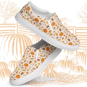 May include: A pair of white slip-on shoes with a repeating pattern of pumpkins, baked goods, and fall foliage. The shoes have a white sole and a cream-colored background. The design includes orange, brown, and beige elements.
