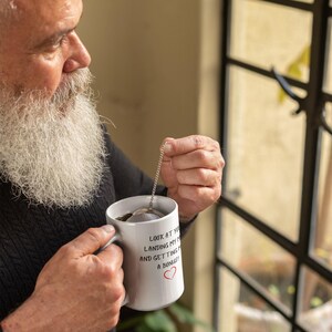 Pu&ograve; includere: Una tazza in ceramica bianca con testo nero che recita "Guardati, stai atterrando il mio aereo e mi stai facendo un bonus!" con un cuore rosso. Una persona tiene la tazza e un infusore per il t&egrave;.