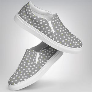 May include: Gray slip-on shoes with a white sole and a pattern of white teeth with yellow accents. The shoes have a white elastic panel on the top and a white interior. The shoes are shown in a floating position.