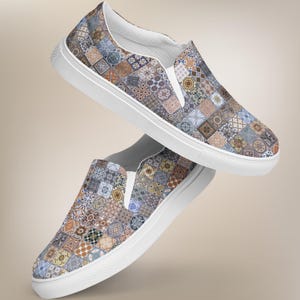 May include: A pair of white canvas slip-on shoes with a colorful patterned design featuring a patchwork of geometric shapes and designs in shades of blue, brown, and beige.