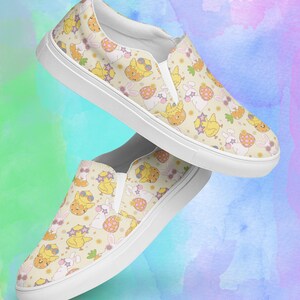 Puede incluir: Un par de zapatos de lona blancos con un fondo amarillo y un patrón de pollitos y conejos de dibujos animados con gafas de sol. Los zapatos tienen una suela blanca y un patrón amarillo y blanco.