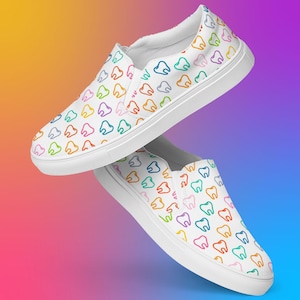 May include: White slip-on shoes with a repeating pattern of colorful teeth. The teeth are outlined in various colors, including blue, green, yellow, orange, and pink. The shoes have a white sole and a white upper.