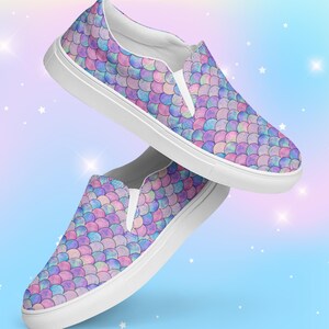 May include: A pair of white slip-on canvas shoes with a mermaid scale pattern in shades of pink, purple, and blue. The shoes have a white rubber sole.
