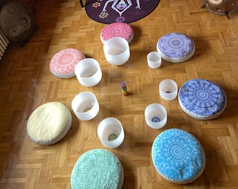 Op de afbeelding: Een set kristallen zangkommen gerangschikt in een cirkel op kleurrijke, gepatroneerde kussens. De kommen zijn van verschillende grootte en worden omringd door een mandala-achtig ontwerp op de vloer.