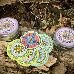Peut inclure: Un jeu de mémoire de mandalas coloré dans une boîte en métal. La boîte est rose avec les mots "Mandala memory game Harmony of the Universe" imprimés dessus. Les cartes sont rondes et présentent des motifs complexes aux couleurs vives.