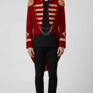 May include: A red military-style jacket with gold trim, epaulets, and decorative buttons. The jacket has a high collar and a tailcoat design. The person is wearing a black t-shirt and black pants. The jacket is a striking piece of apparel.