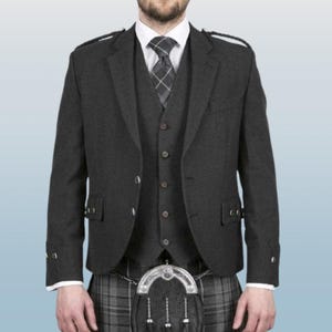 Puede incluir: Una chaqueta de kilt gris oscuro con un chaleco a juego y una falda escocesa a cuadros. La chaqueta tiene un cierre de un solo botón y una solapa de muesca. El chaleco tiene un cierre de botones y un bolsillo en el pecho. La falda escocesa es una prenda tradicional escocesa con una falda plisada y un broche de kilt.