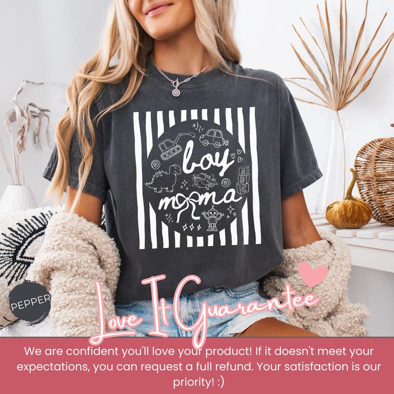 May include: Dark gray t-shirt with a white graphic that says "boy momma" with illustrations of a dinosaur, car, and other toys. The shirt has a relaxed fit and is worn by a person.
