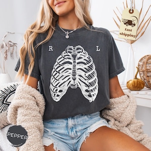 May include: Dark gray t-shirt featuring a white rib cage graphic. The shirt has the letters "R" and "L" printed above the rib cage design. The shirt is made of a soft material.