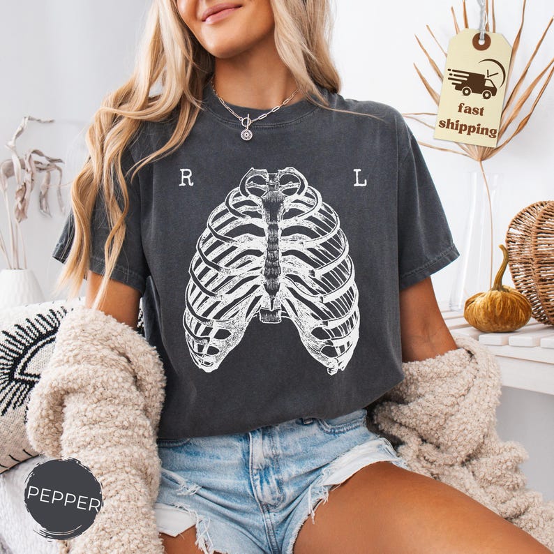 May include: Dark gray t-shirt featuring a white rib cage graphic. The shirt has the letters "R" and "L" printed above the rib cage design. The shirt is made of a soft material.