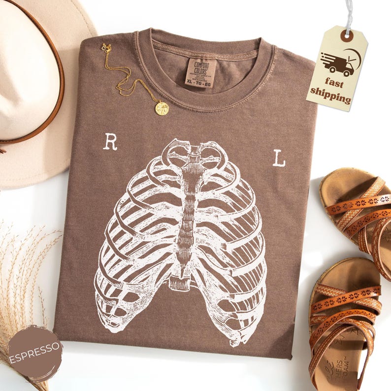 May include: Espresso-colored t-shirt with a white rib cage graphic. The shirt has the letters "R" and "L" printed on it. A gold necklace and brown sandals are also in the image. A tag with "fast shipping" is attached.