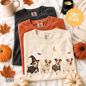 May include: Three crewneck t-shirts in charcoal, burnt orange, and ivory. The ivory shirt features a graphic of four Jack Russell Terriers dressed in Halloween costumes, including a witch, mummy, zombie, and ghost, with stars and a crescent moon.