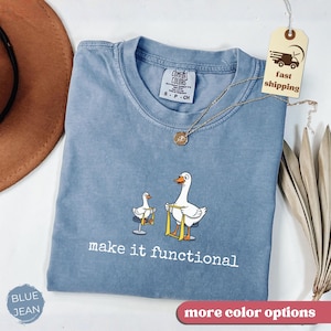May include: Blue jean colored t-shirt with a crew neck. The shirt features a graphic of two white geese with yellow straps and the text "make it functional". A gold necklace and a tag that says "fast shipping" are also visible.