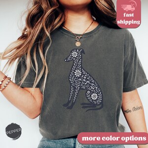 May include: A dark gray t-shirt with a floral design of a dog. The dog is outlined in black and the flowers are white. The word "Cooper" is spelled out in the flowers. The shirt has a crew neck and short sleeves.
