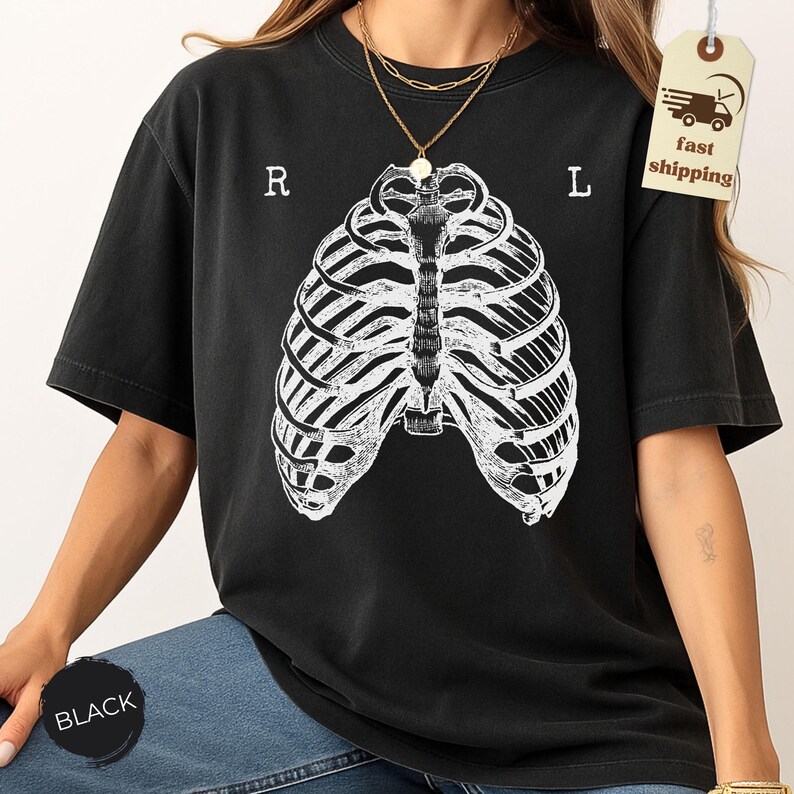 May include: Black t-shirt featuring a white rib cage graphic. The letters "R" and "L" are printed above the rib cage. The shirt is a relaxed fit and has short sleeves. The word "BLACK" is printed on a black circle.