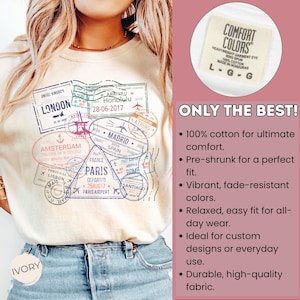 May include: Ivory-colored Comfort Colors t-shirt featuring travel-themed stamps from cities like London, Paris, and Amsterdam. The shirt includes the text "ONLY THE BEST!" and details about the fabric.